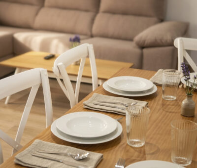 Comedor de apartamento rural en Puerto Lápice con mesa de madera, menaje completo y salón al fondo.