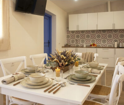 Salón comedor con mesa puesta y cocina equipada en apartamento rural de Puerto Lápice.