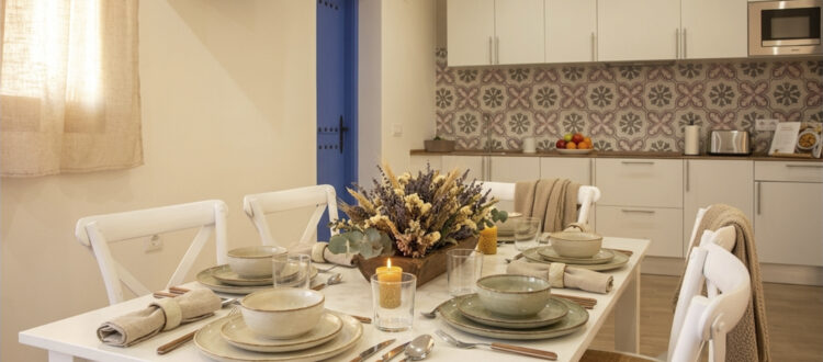 Salón comedor con mesa puesta y cocina equipada en apartamento rural de Puerto Lápice.