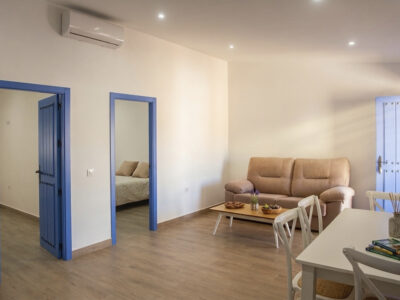 Salón comedor amplio con sofá beige, aire acondicionado y puertas azules en apartamento rural de Puerto Lápice.