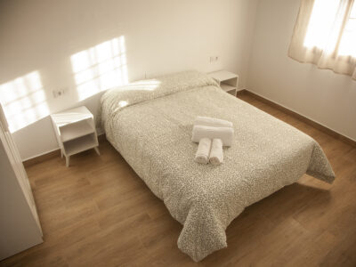 Dormitorio luminoso con cama doble y suelo porcelánico efecto madera en alojamiento de Puerto Lápice.