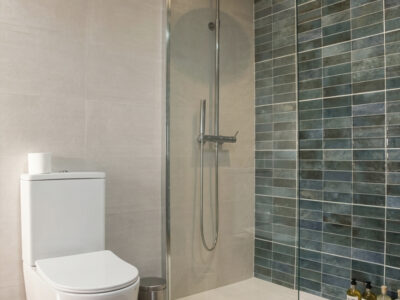 Baño moderno con ducha de plato grande y azulejos turquesa en casa rural de Puerto Lápice.